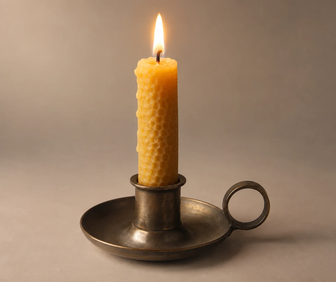 Lit beeswax candle in a plain metal holder.