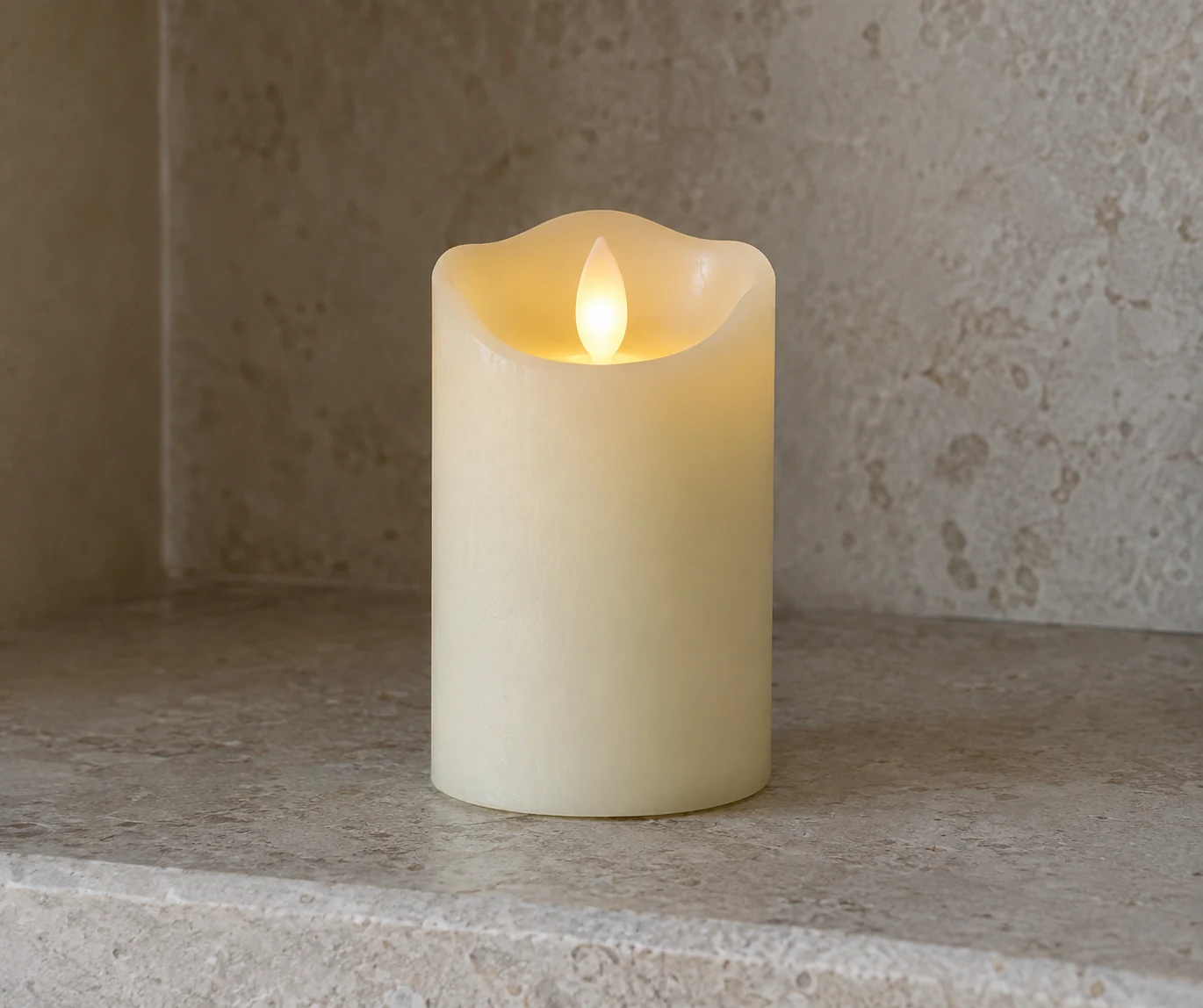 An ivory flameless candle with a faux flame stands alone on a stone shelf.