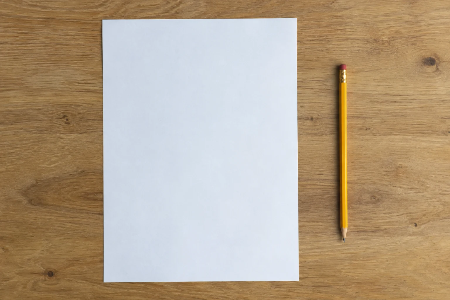 A blank sheet of paper and a pencil lie on a wooden table.