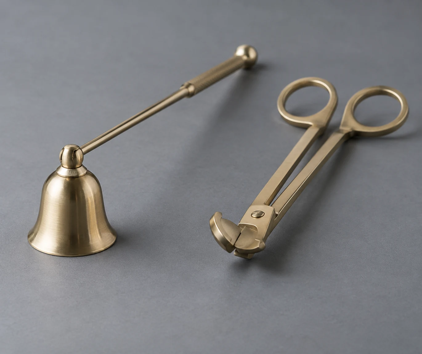 A modern bell-shaped candle snuffer beside wick-trimming scissors on a gray surface.