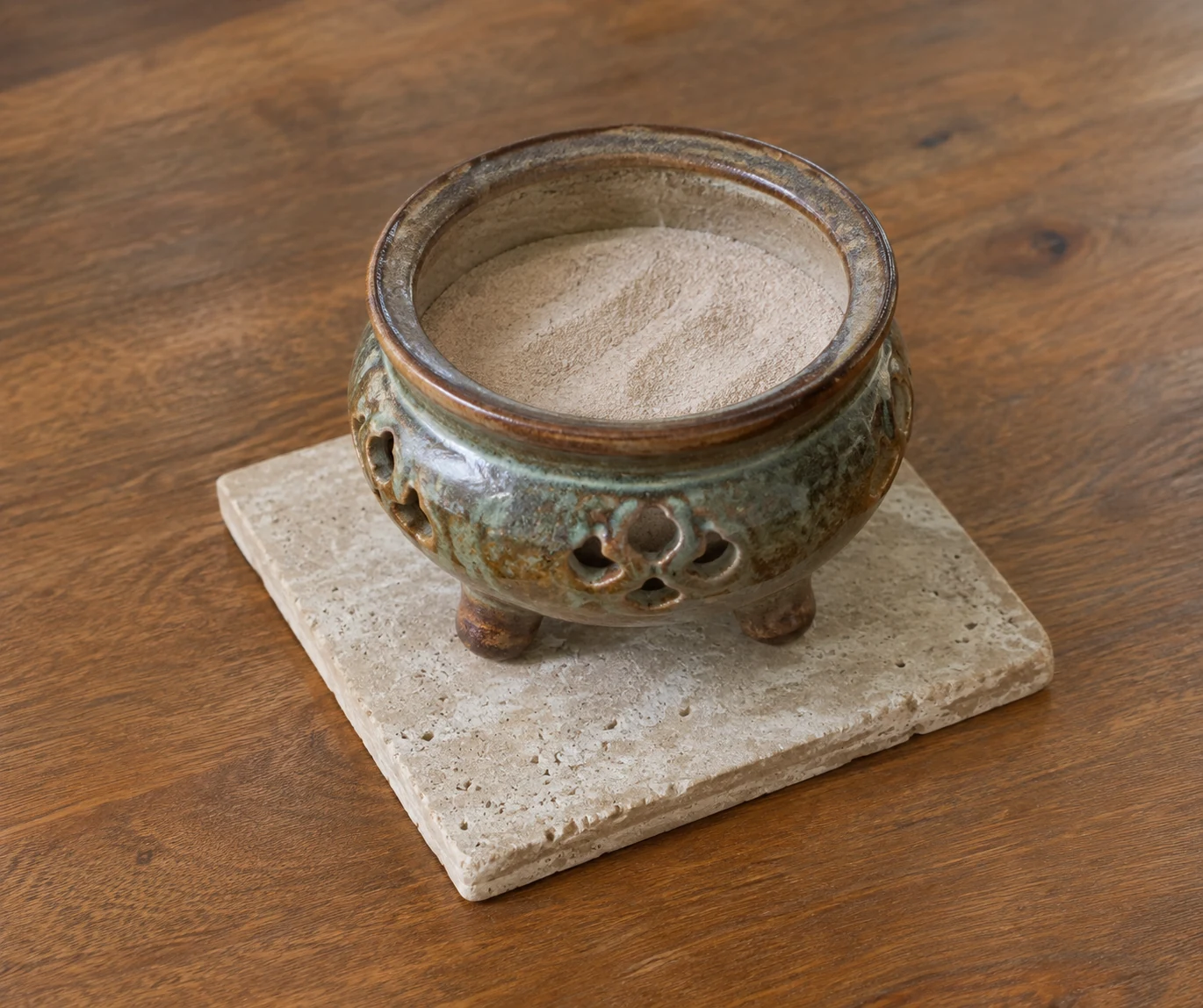 An empty sand-filled ceramic burner on a stone tile above a wooden table.
