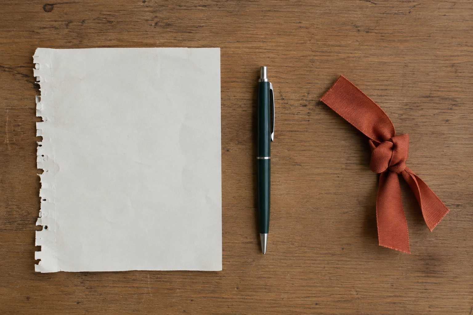 Reused paper, a pen, and knotted ribbon arranged separately on a desk.