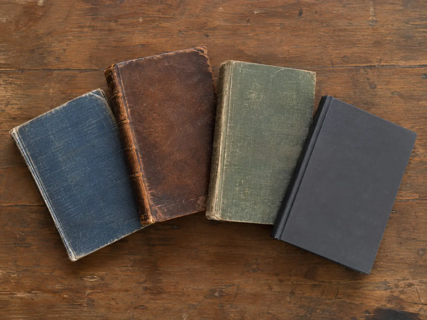 Four unmarked books with varied old and modern bindings arranged on a wooden table.