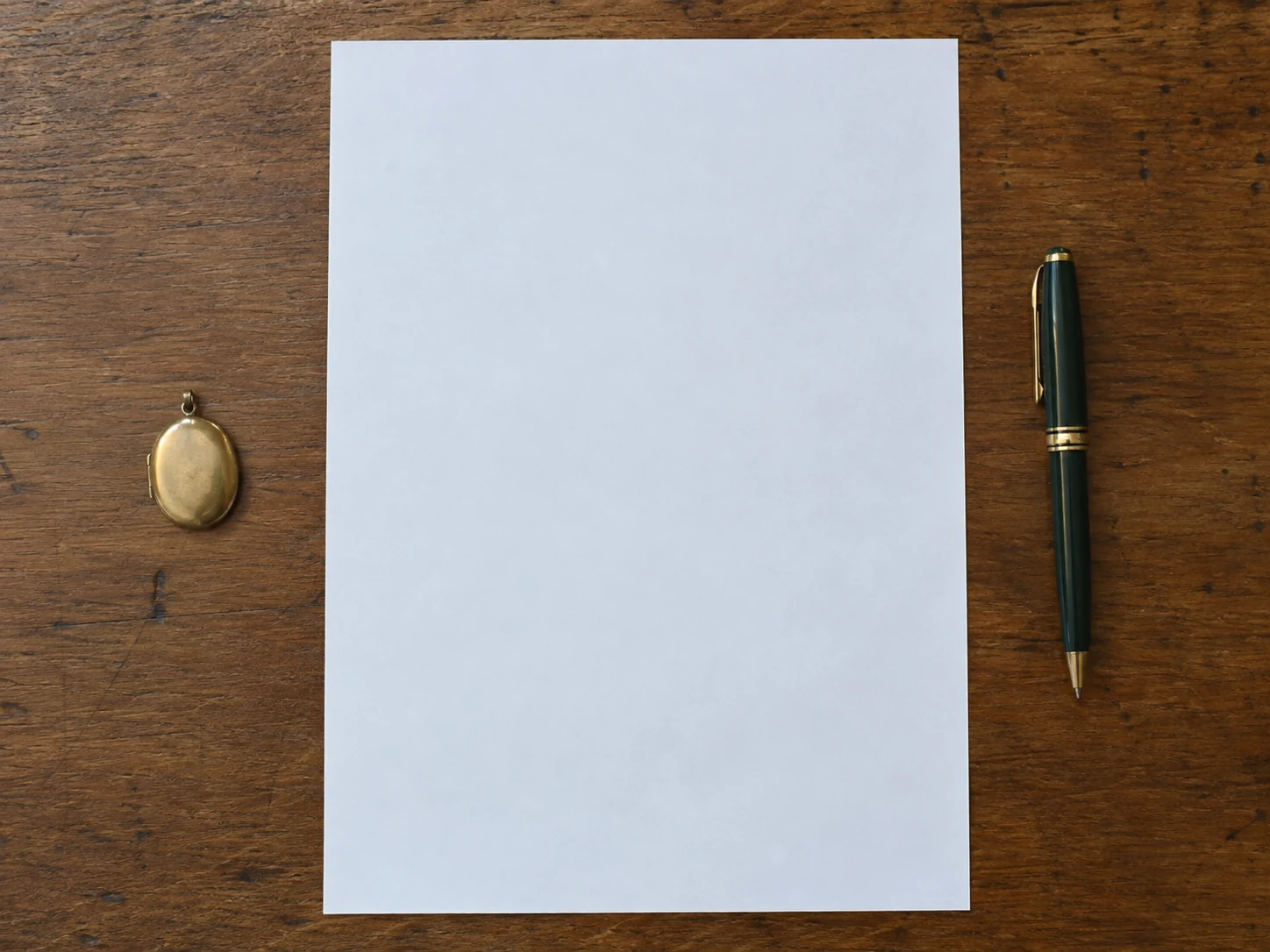 A closed locket, blank paper, and a pen laid out on a table.