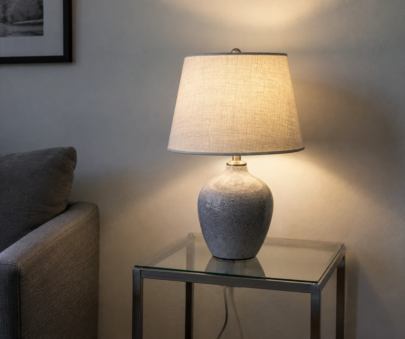 A lit table lamp on a clear side table, casting light on the wall.