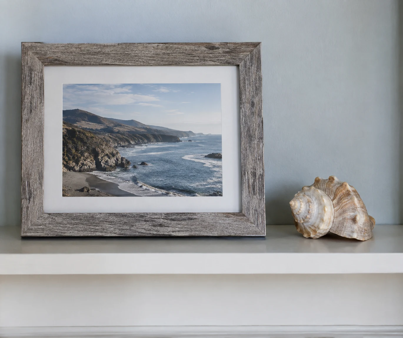 A coastal photograph and a seashell on a shelf as a simple personal remembrance space.