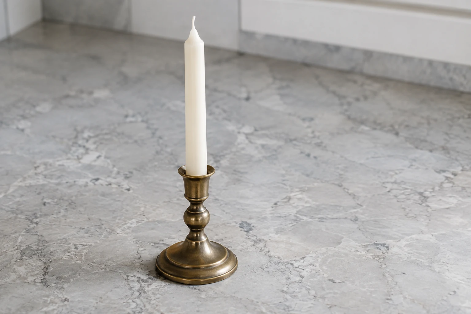 Unlit candle standing in a sturdy holder on a clear stone surface.