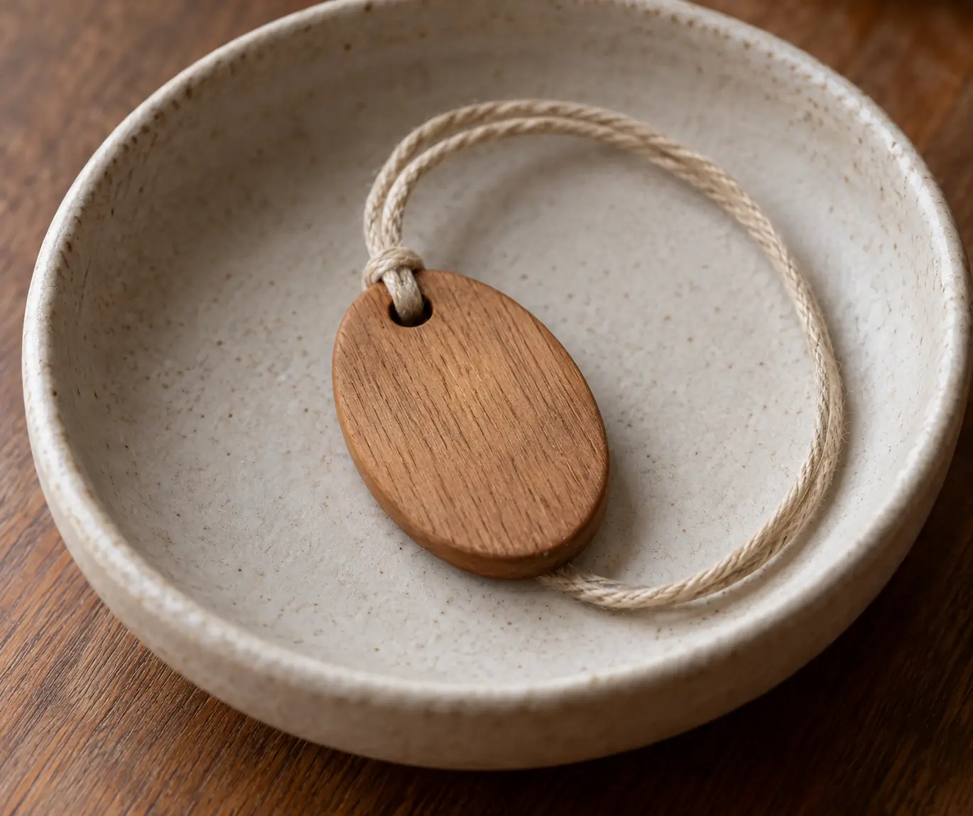 Unmarked wooden pendant and cotton cord resting in a shallow ceramic dish.