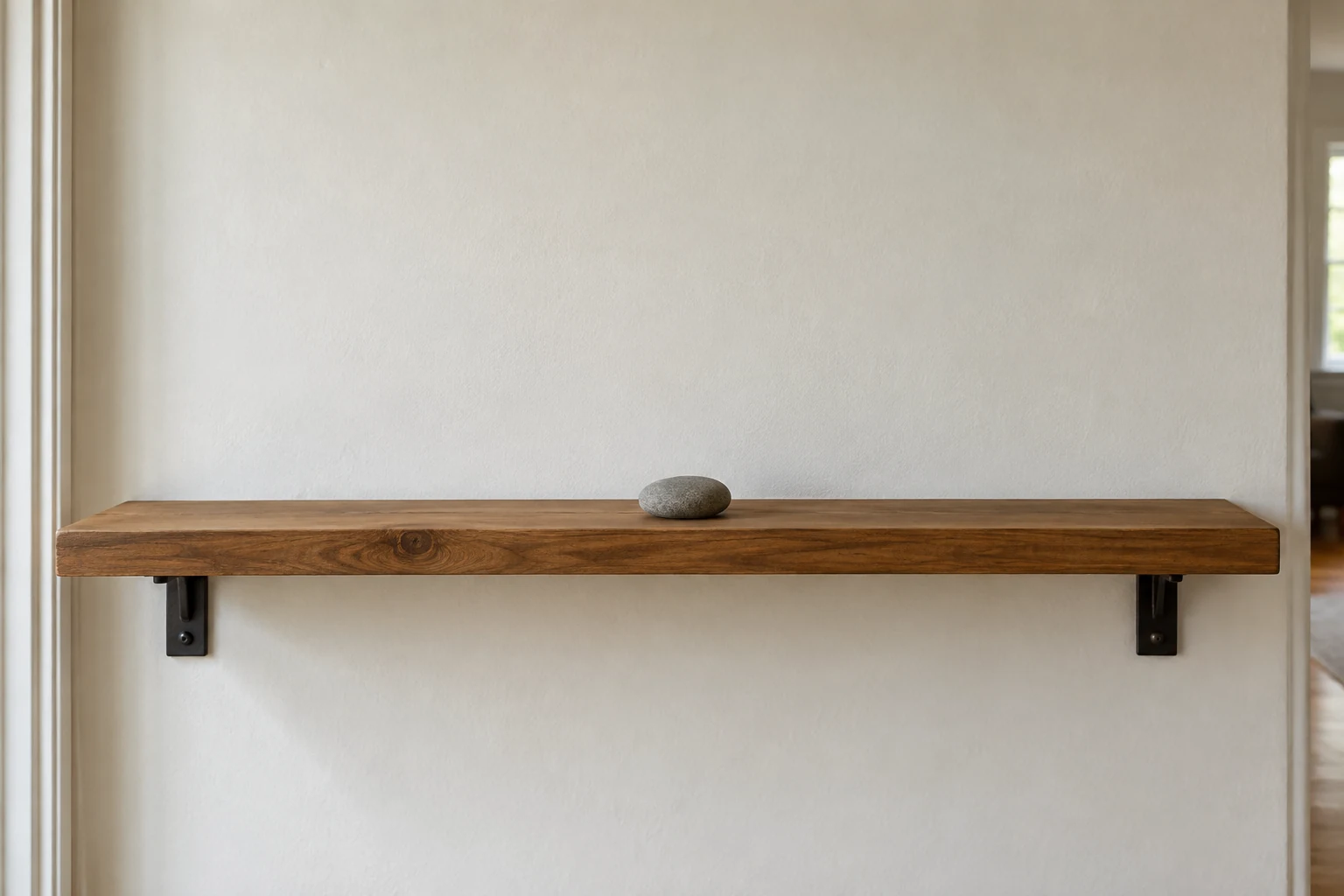 One smooth stone on an otherwise clear wooden shelf at home.
