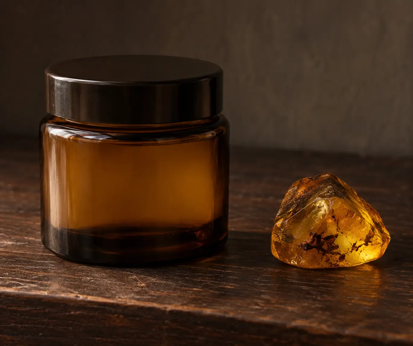 An unlabeled amber-glass fragrance jar beside a separate translucent fossil amber specimen on a dark altar surface.