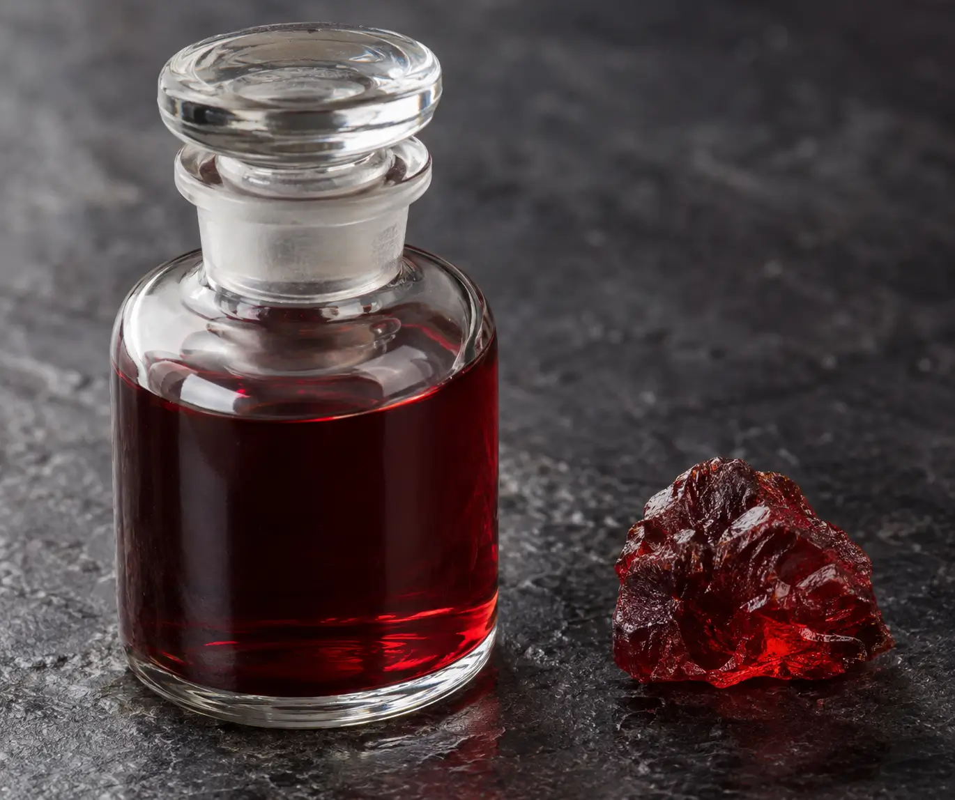 Unlabeled glass bottle of dark red liquid beside a single piece of red resin.