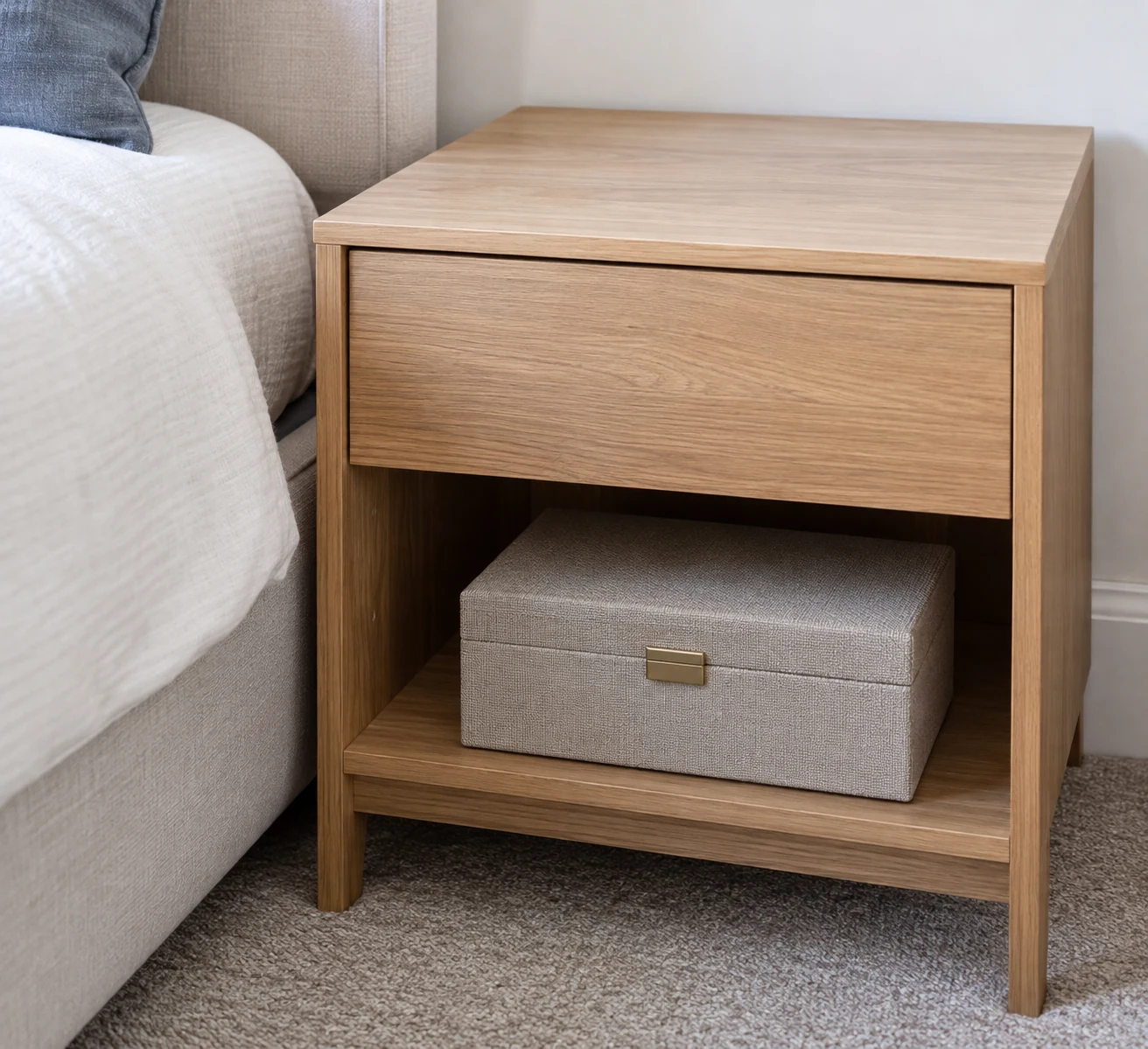 A closed keepsake box rests on the lower shelf of a bedside cabinet with a clear tabletop.
