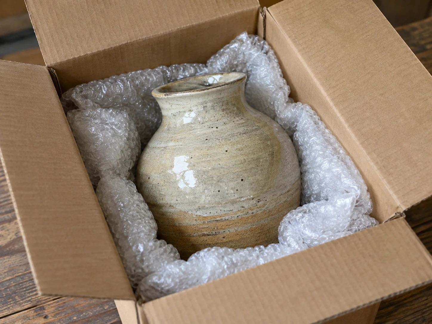 A ceramic vessel rests in cushioning inside an open packing box on a table.