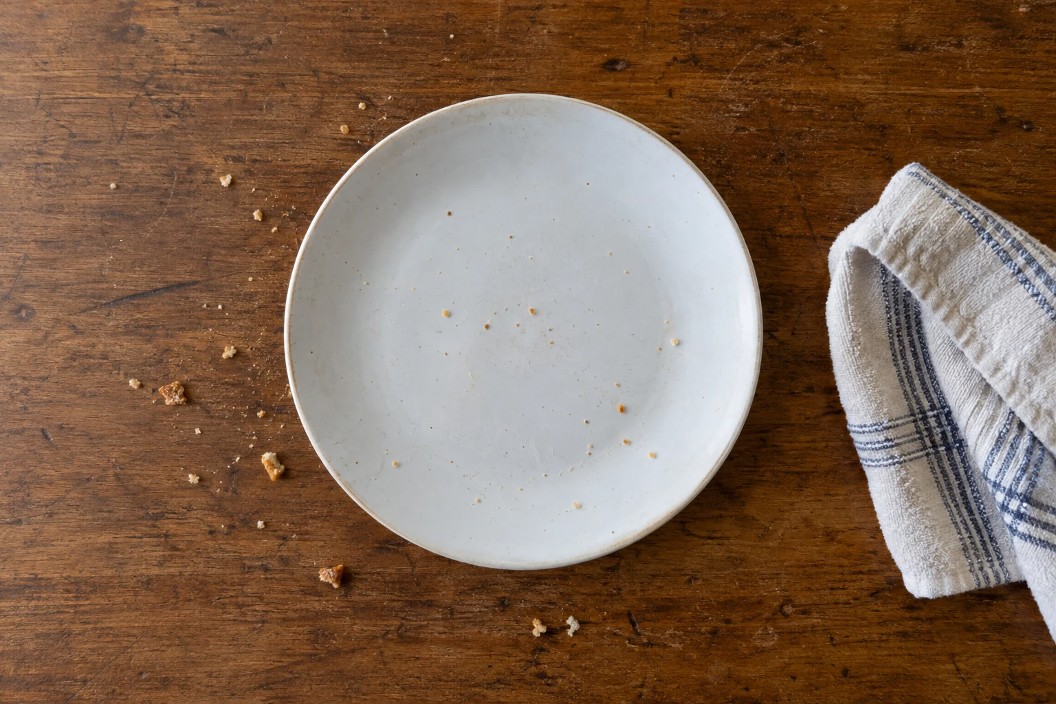 Empty plate with crumbs on the nearby surface and a cleaning cloth to one side.