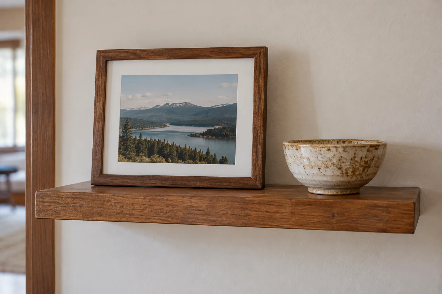 A framed landscape photograph and ceramic bowl rest on a small shelf.