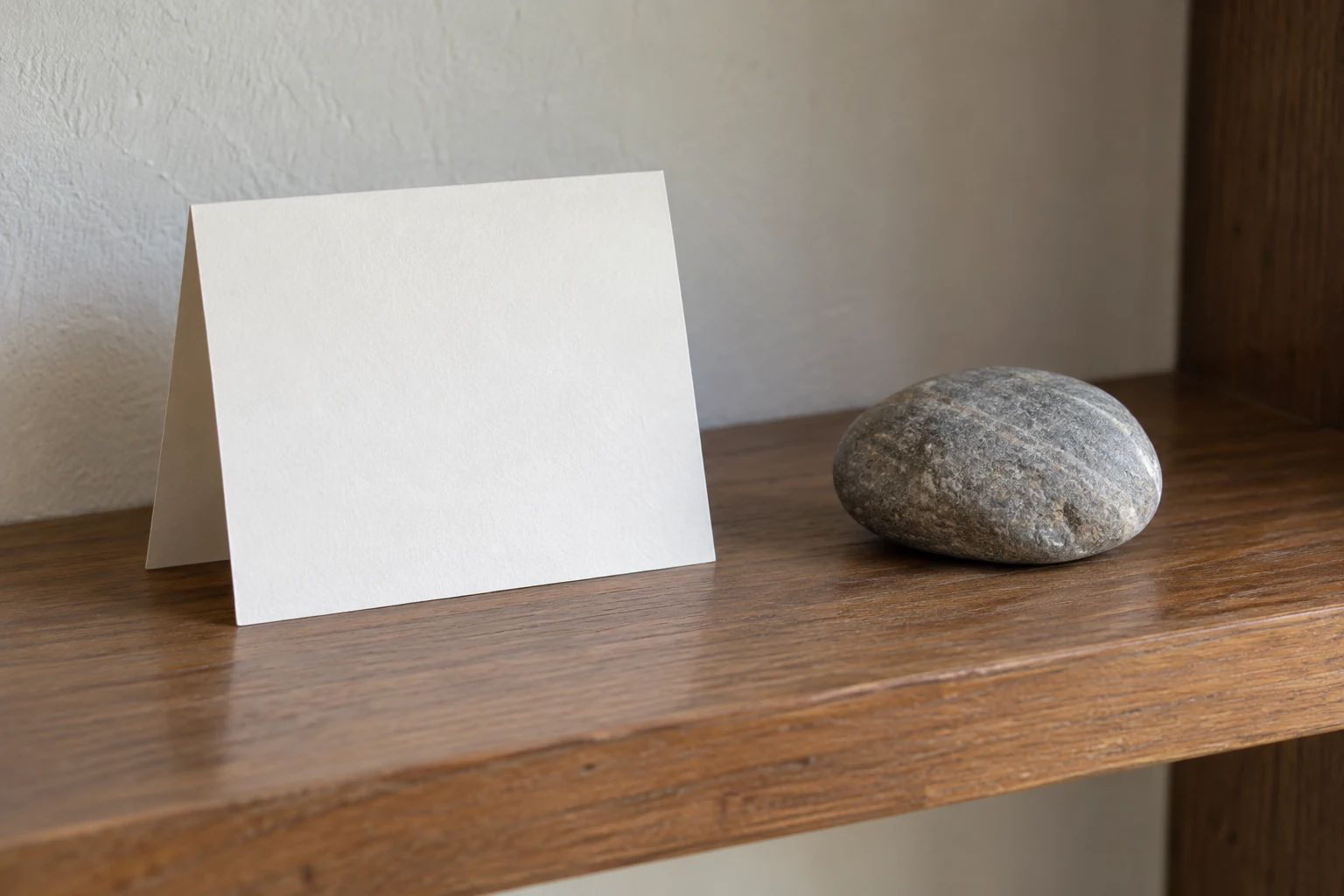 A folded paper card and smooth stone resting separately on a home shelf.